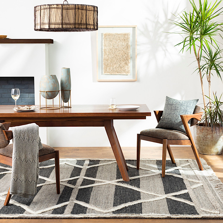A dining room set on top of a gray, black, and cream rug with a geometric pattern.